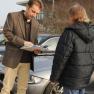 Mann zeigt einemn Mann vor Auto ein Papier
