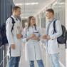 Drei junge Medizin-professionelle in Kitteln, die im Flur eines Krankenhauses sprechen.